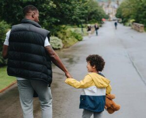 father and son walking through a park in a large city