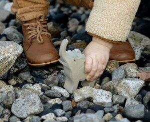 a toddlers shoes standing on rocks while playing with a toy elephant